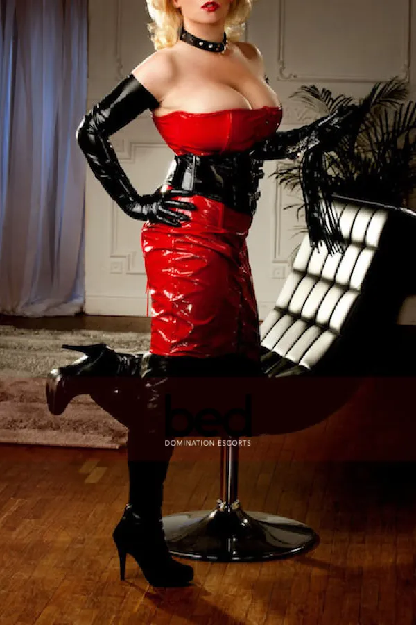 Mistress Charlotte kneeling on a chair wearing a red latex dress