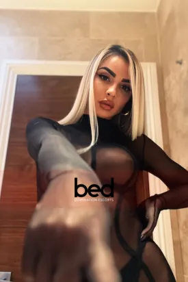 Mistress Julia pointing at the camera while she stands in a seethrough bodysuit 